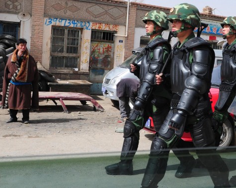 A Tibetan man (L) in traditional clothing watches as Chinese paramilitary troops in riot gear march along the streets of Guomaying in northwest China's Qinghai province, in a vast region on the Tibetan Plateau known as Amdo.