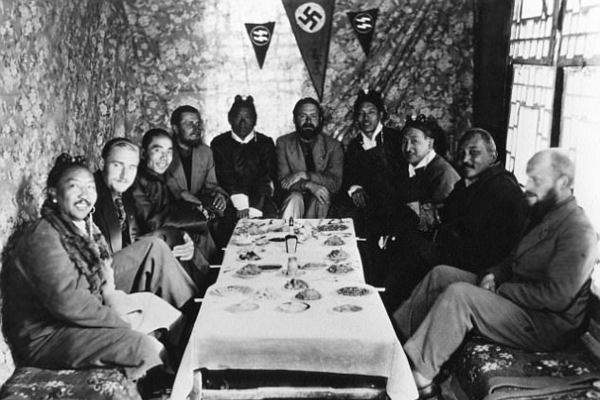 A shot from the Tibetan expedition as the members of the team sit down around a table with locals in a room adorned by a swastika and the SS logo.