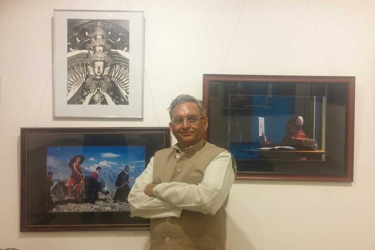 Vijay Kranti poses for a photo before two of his favourite photos he took of the Dalai Lama, at his exhibition in New Delhi, India, on 14 April 2016.