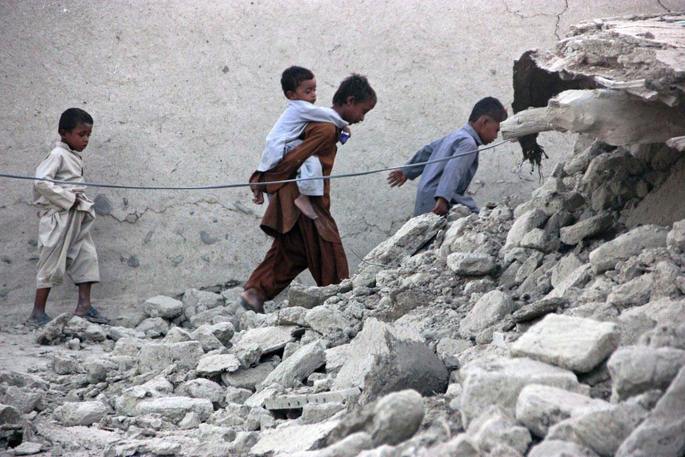 Survivors of an earthquake walk on rubble of a mud house after it collapsed