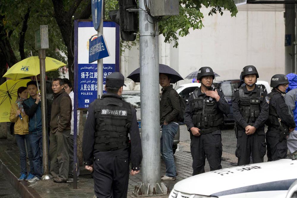 People watch armed policemen standing guard near the site of an explosion in Urumqi, East Turkistan