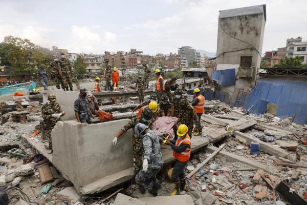 India's National Disaster Response Force personnel and Nepal army soldiers carry a body after being recovered from a collapsed house.