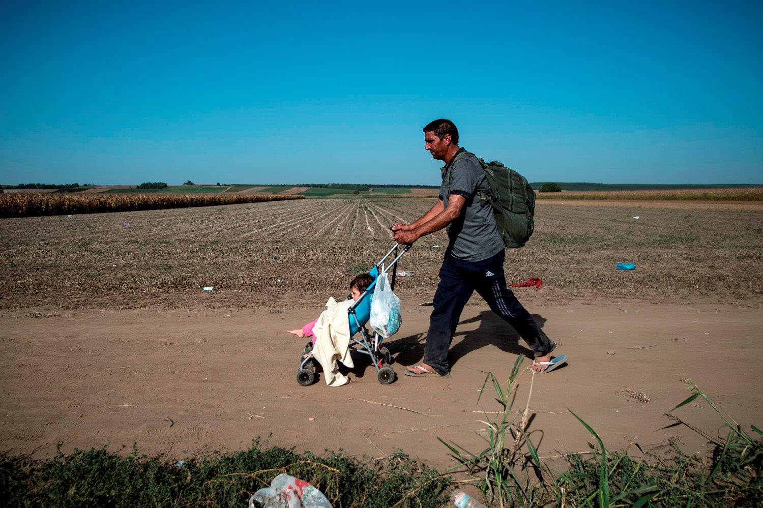 A refugee wheels his child in a pushchair on a dirt road towards the border between Croatia and Serbia, near the western-Serbia town of Sid, on 18 September 2015.
