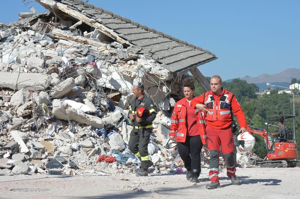 A firefghter and rescuers walk past the rubble of a destroyed building in the damaged central Italian village of Amatrice on 26 August 2016, two day after a 6.2-magnitude earthquake struck the region.