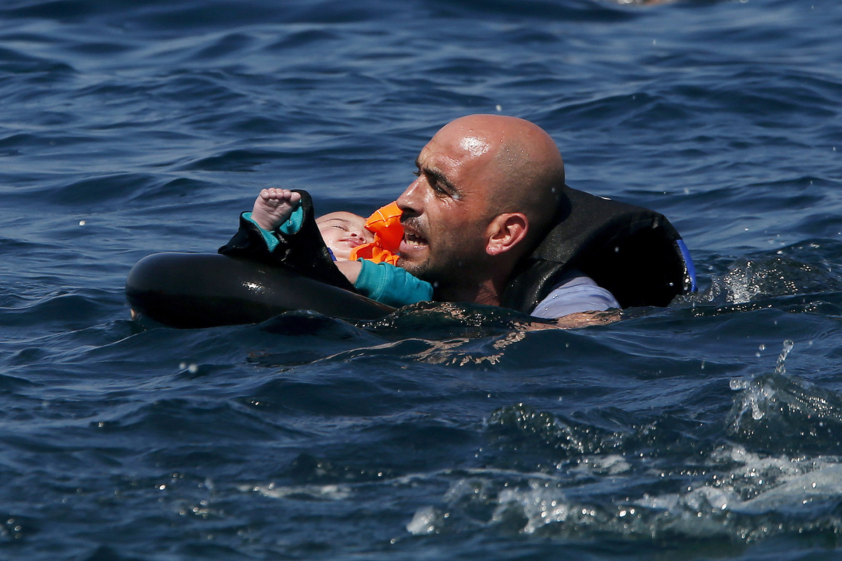 A Syrian refugee holding a baby in a lifetube swims towards the shore after their dinghy deflated some 100m away before reaching the Greek island of Lesbos, on 13 September 2015.
