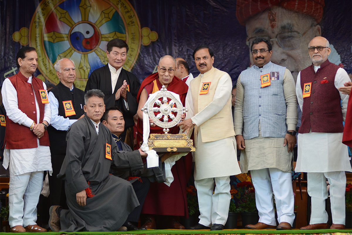 The Dalai Lama presenting a memento to the Culture Minister of India Mahesh Sharma during the 'Thank You India' event at Tsuglakhang temple  in McLeod Ganj, India, on 31 March 2018. Also seen from left:  Food Minister of Himachal Pradesh Kishen Kapoor; Member of Parliament Shanta Kumar; and CTA President Lobsang Sangay. From right: Member of Parliament Satyavarath Chaturvedi; and BJP General Secretary Ram Madhav. Kneeling are CTA Finance Minister Karma Yeshi and Health Minister Choekyong Wangchuk.