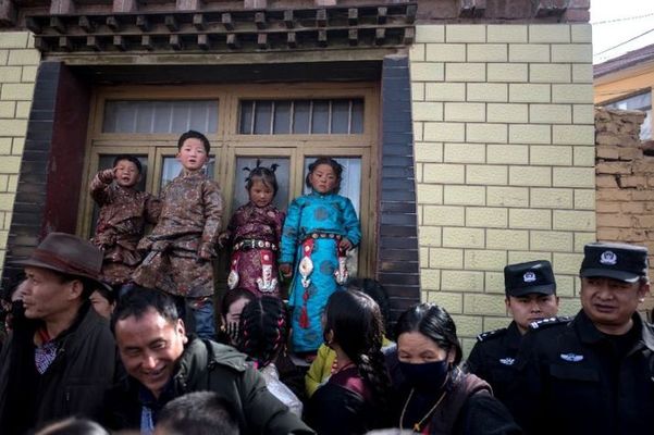 Children in traditional Tibetan clothes and police watch passing Tibetan Buddhist monks during a ceremony in March 2018.