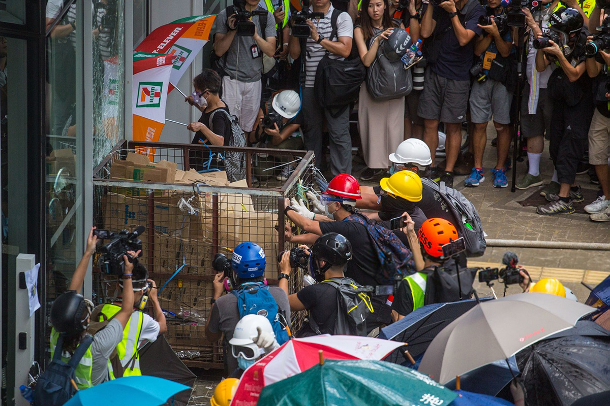 Protesters try to push a metal cart through a closed entrance at the government headquarters in Hong Kong on 1 July 2019, on the 22nd anniversary of the city's handover from Britain to China. Anti-government protesters smashed windows of Hong Kong's Legislative Council on 1 July and were trying to force their way into the building by ramming a metal cart through the glass doors, as police responded with pepper spray.