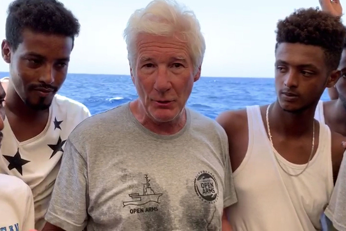 An image grab taken from a video released by the Spanish NGO Proactiva Open Arms on 9 August 2019 shows US actor Richard Gere (C) speaking on board the charity's boat transporting 121 migrants rescued from the middle of the Mediterranean Sea and waiting for a port to dock at.