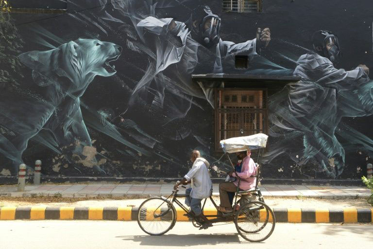 A rickshaw driver carries passengers wearing facemasks past a mural in the Lodhi Art District in New Delhi.