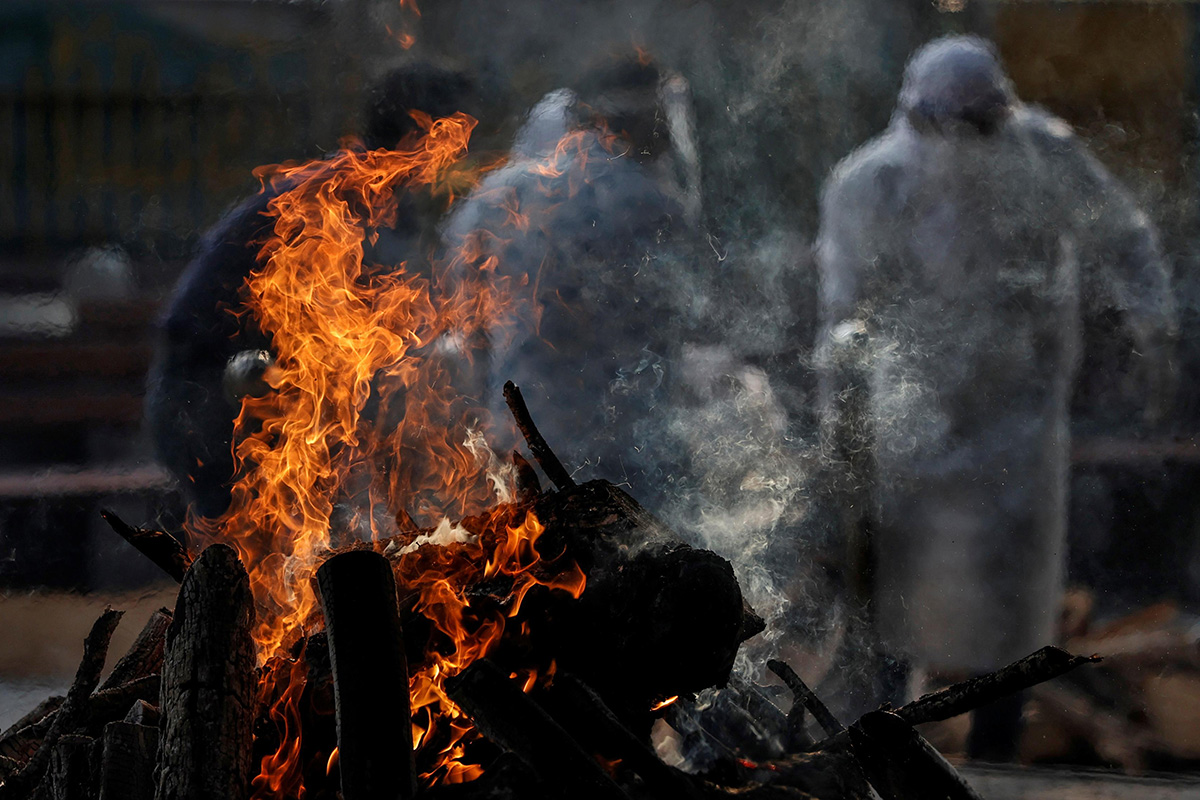 A burning pyre of a man who died due to the coronavirus disease (COVID-19), is seen as another one is carried for cremation at a crematorium in New Delhi, India, on 3 June 2020.