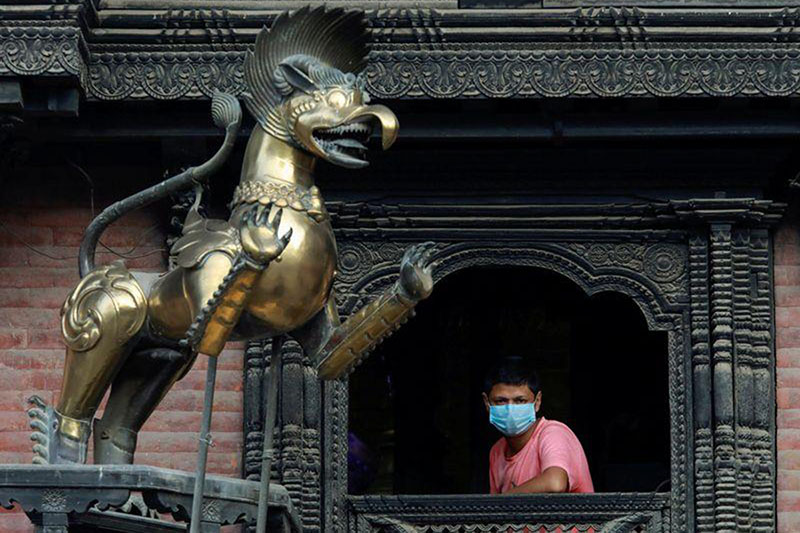 A man wearing a protective face mask looks through the window of a temple amid the spread of coronavirus disease (COVID-19), in Kathmandu, Nepal, on 9 October 2020.