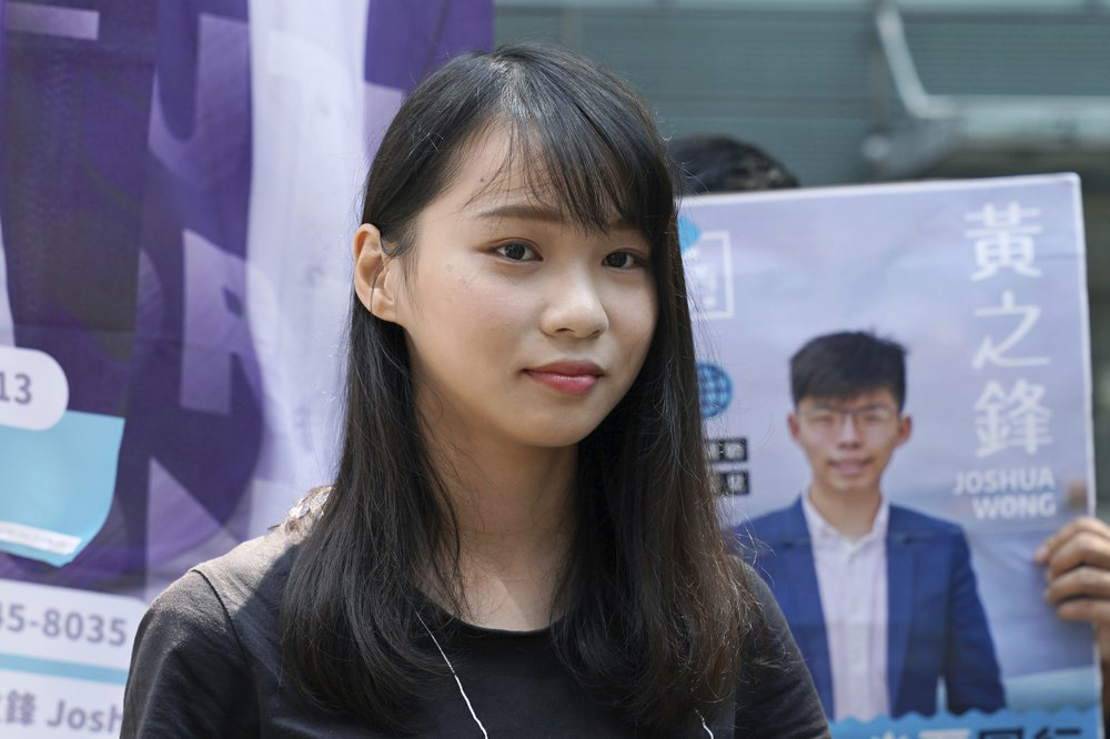 In this 28 September 2019 photo, Hong Kong pro-democracy activist Agnes Chow, stands next to an election campaign poster of pro-democracy activist Joshua Wong, in Hong Kong. Chow and activist Ivan Lam have been sentenced to jail on Wednesday, over charges related to an unauthorized anti-government protest last year at the city's police headquarters.