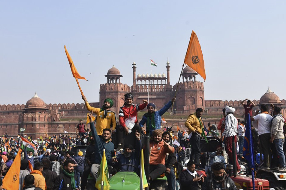 Sikhs wave the Nishan Sahib, a Sikh religious flag, as they arrive at the historic Red Fort monument in New Delhi, India, on 26 January 2021. Tens of thousands of protesting farmers drove long lines of tractors into India's capital on Tuesday, breaking through police barricades, defying tear gas and storming the historic Red Fort as the nation celebrated Republic Day.
