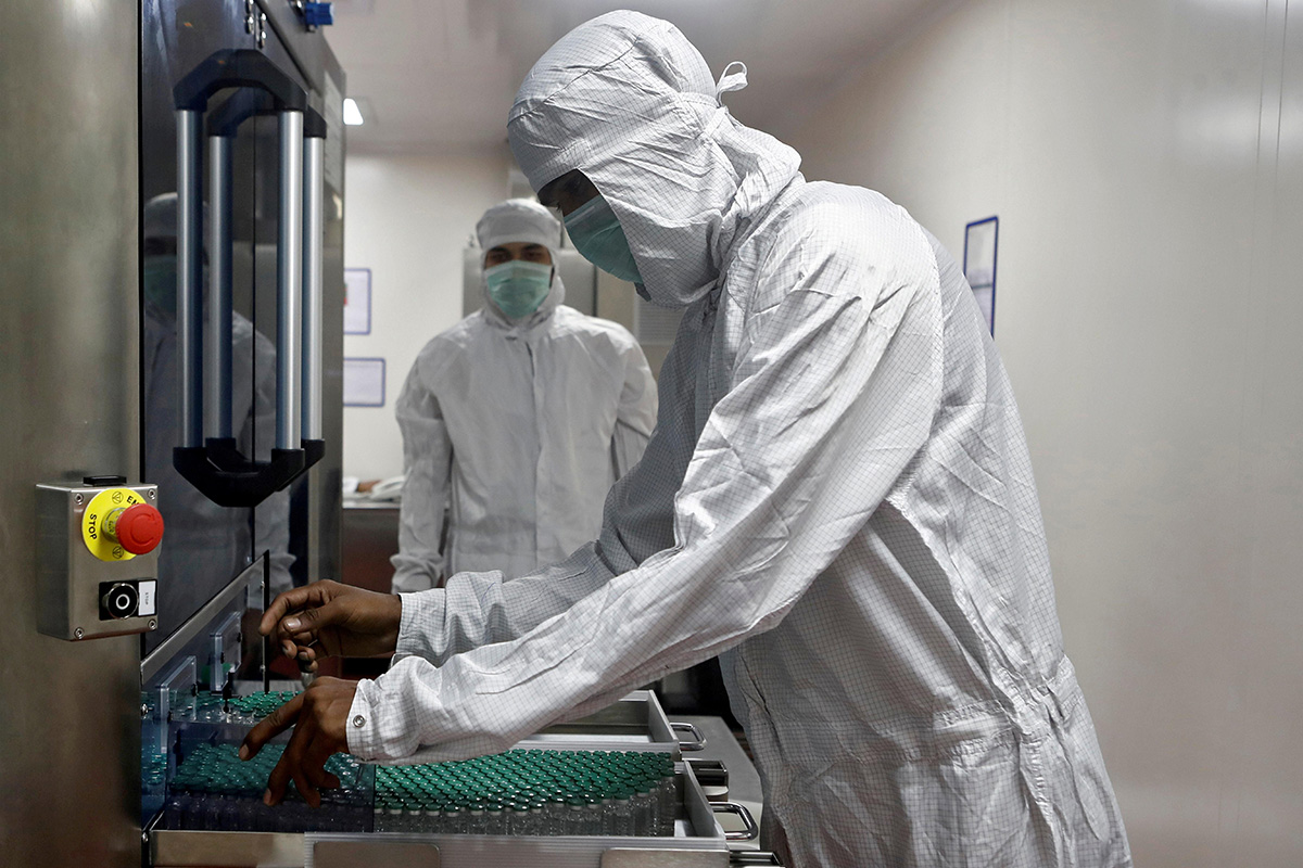 An employee in personal protective equipment (PPE) removes vials of AstraZeneca's COVISHIELD, coronavirus disease (COVID-19) vaccine from a visual inspection machine inside a lab at Serum Institute of India, Pune, India, on 30 November 2020.