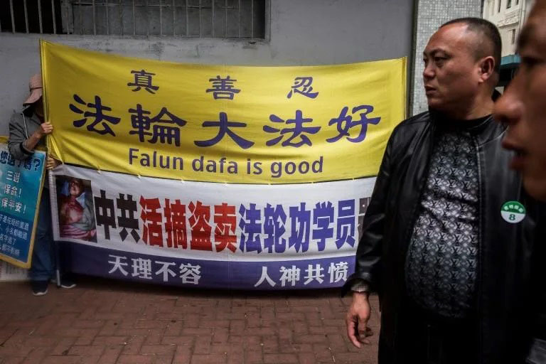 A Falun Gong activist holds a sign in January 2021 next to a tour group from mainland China, where repression of the spiritual group prompted US sanctions on a former official.