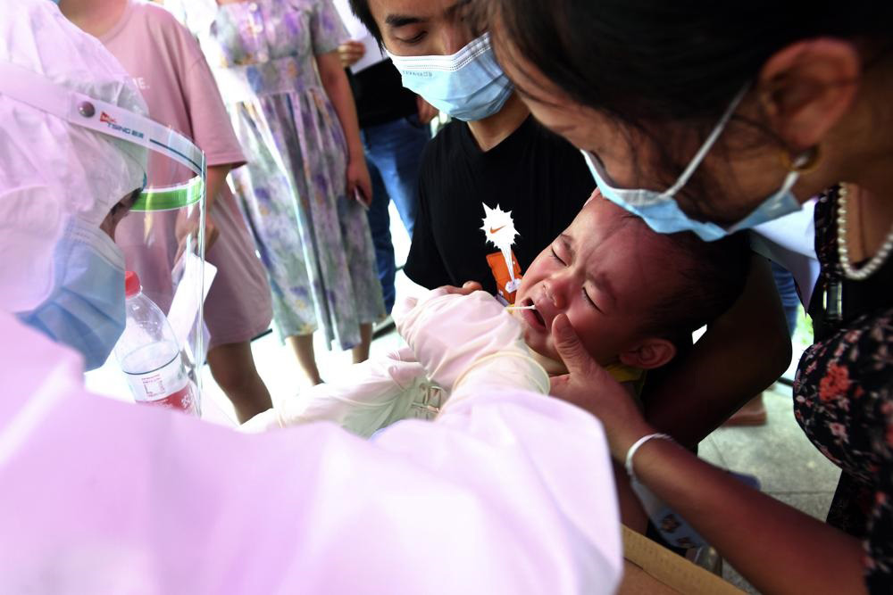 A medical worker takes swab samples from a child during mass testing for COVID-19 at a residential block in Wuhan in central China's Hubei province on 3 August 2021. China suspended flights and trains, canceled professional basketball league games and announced mass coronavirus testing in Wuhan on Tuesday as widening outbreaks of the delta variant reached the city where the disease was first detected in late 2019.