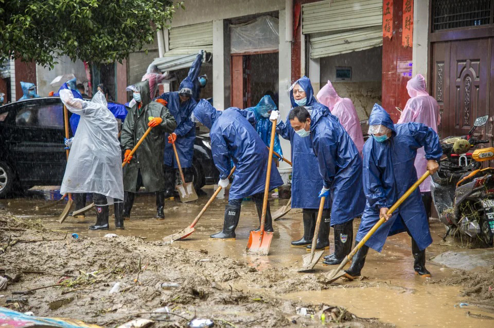In this photo released by China's Xinhua News Agency, people shovel debris and mud from a road in Liulin Township of Suixian County in central China's Hubei Province, on 13 August 2021. Flooding in central China continued to cause havoc in both cities and rural areas, with authorities saying Friday that more than 20 people had been killed and another several were missing.